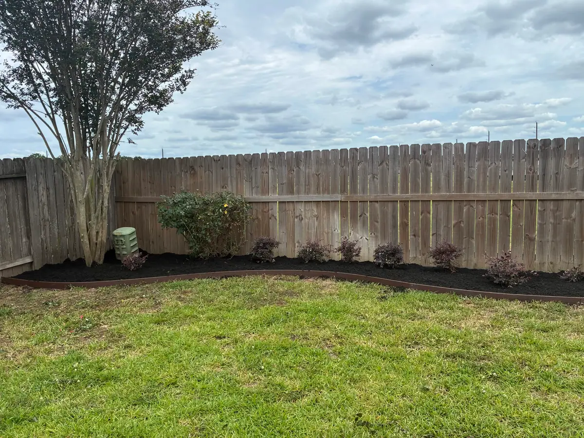 Long backyard border bed planted along a wood privacy fence