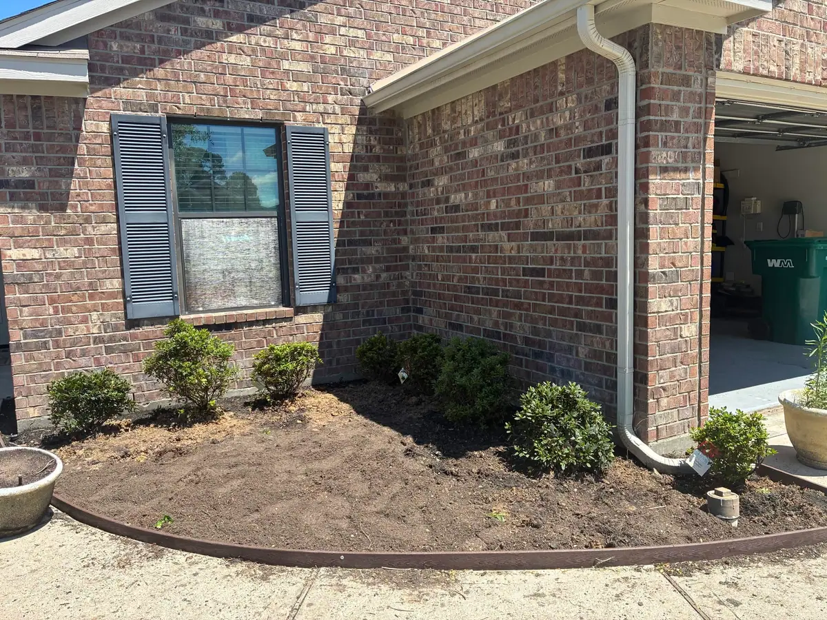 Corner flower bed with newly planted azaleas beside a brick garage