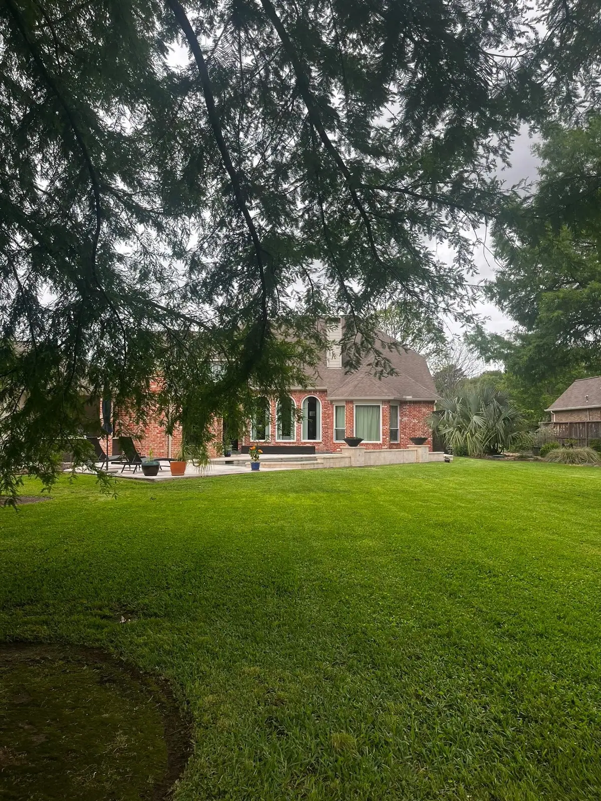 Healthy deep-green lawn under mature trees at a large brick home